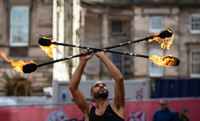 Performer holds fiery staffs in a cross, highlighting their face