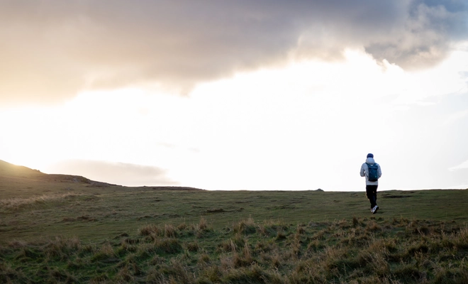 A man with his back to the viewer walks towards a sun setting over the horizon