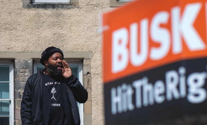A performer making an announcement - next to a sign saying 'BUSK'