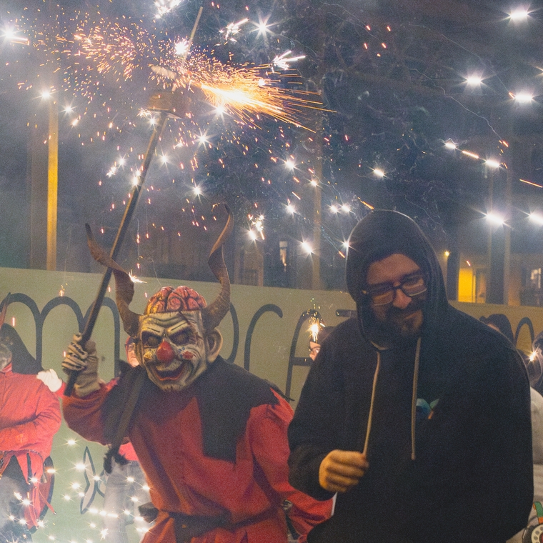 A masked devil sneaks up on unaware bystander shielding themselves from sparks